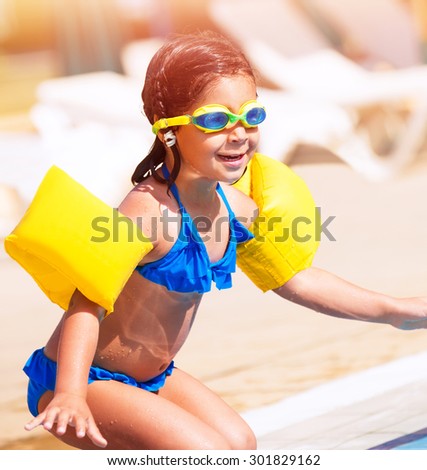 Little girl on the beach, having fun near swimming pool and preparing to jump into the water, spending summer holidays on beach resort