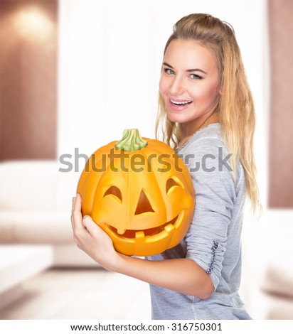 Beautiful blond girl celebrate Halloween holiday at home, holding in hands carved pumpkin face, enjoying happy autumn holiday