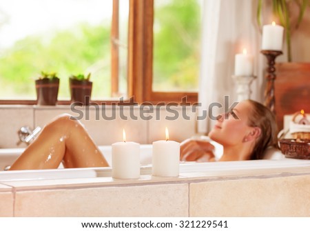 Soft focus photo of gentle young woman lying down in bath tub with foam and candle, enjoying spa procedure in the luxury resort