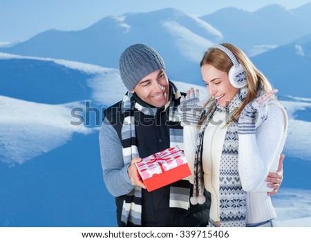 Handsome cheerful man giving to her precious girlfriend red gift box, celebrating Christmas holidays in the beautiful snowy mountains