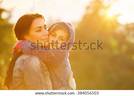 Portrait of beautiful mother with love hugging her precious daughter in bright yellow sunlight in the park, happy family life