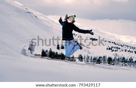 Cheerful woman jumping in the mountains covered with snow, spending winter holidays on the ski resort, enjoying winter vacation, happy active lifestyle