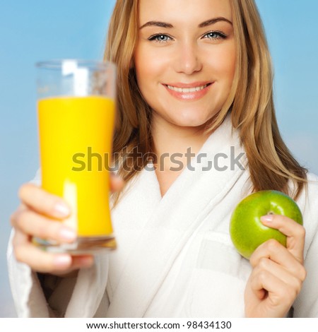Healthy lovely young woman dieting, beautiful girl holding orange juice and green fresh apple fruit, happy smiling female portrait outdoor over blue sky background, nutrition and wellness concept