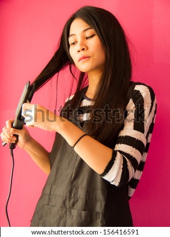 Asian girl dressing her hair with hair straighteners.