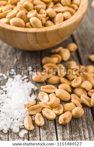Salted roasted peanuts and salt on old wooden table.