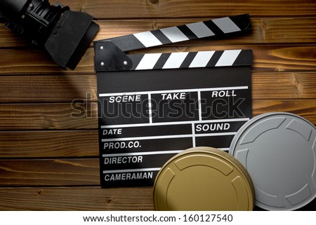 top view of clapper board with movie light and film reels on wooden table