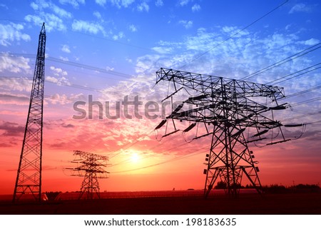 The setting sun under stands the shapes of high voltage towers in the fields