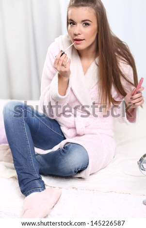 Young long-haired blonde girl in a bathrobe , lips gloss paints siting on the bed