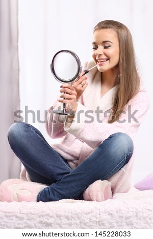 Young long-haired blonde girl in a bathrobe sitting on the bed, lips gloss paints