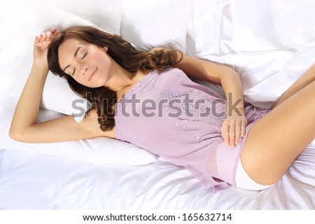 Beautiful woman resting on a soft bed linen / Young girl is resting in a white linen dressed in a purple shirt night