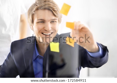 Young, handsome man of success in the office room glued yellow notes . The young director in the blue suit putting up notes