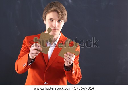 Gold puzzle - a puzzle Business  /   Portrait of a young, handsome man in the orange jacket standing on black background plate