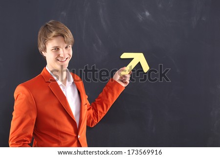 Happy man pointing at the black board  / Portrait of a young, handsome man in the orange jacket standing on black background plate