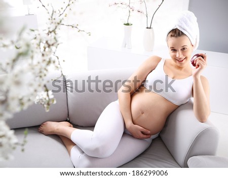 Diet in pregnancy . Pregnant woman relaxes on the sofa, drinking juice and cradled naked pregnancy belly