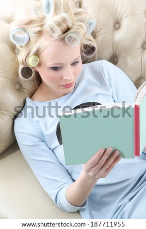 Relax with a nice book.  Young woman with hair rollers screwed reading a book while relaxing on the sofa