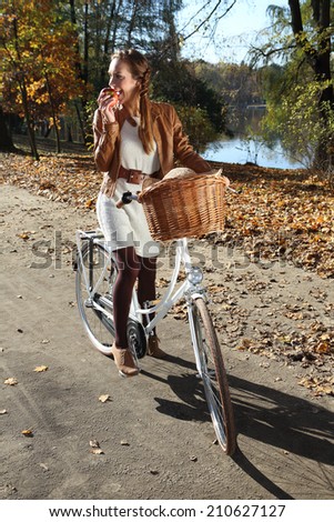 Autumn bike tour. Girl eating an apple on the background of autumn, orange park