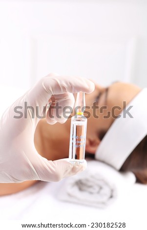 Vitamin cocktail applied to the face.Gloved hand medical shows ampoule with a cosmetic preparation, in the background a woman waiting for surgery