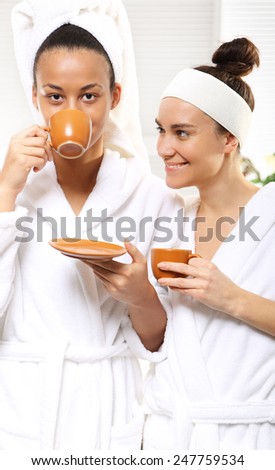 Coffee, relaxation and beauty woman in a beauty salon. Two women in wellness salon dressed in white robes with cups of coffee