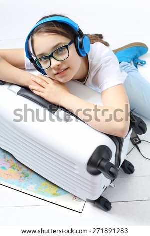 Your journey of dreams.
Girl in blue headphones packed suitcase with things for a holiday trip