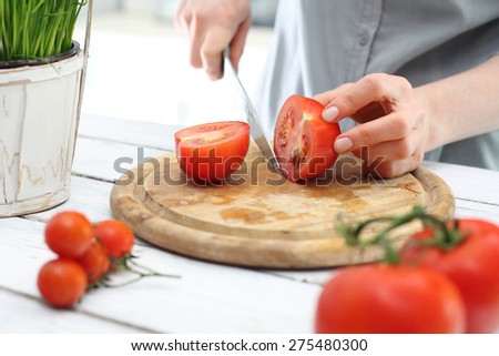 Red vegetables, tomatoes in the kitchen. Hands woman standing in the kitchen while chopping tomatoes