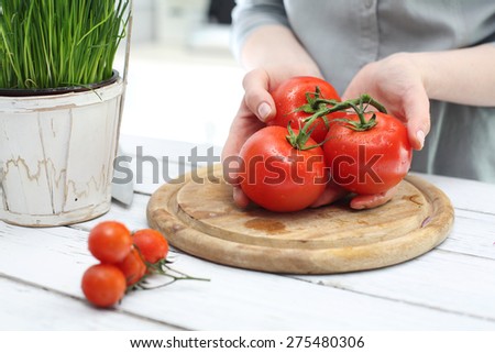 Female different species shows tomatoes. Hands woman standing in the kitchen while chopping tomatoes