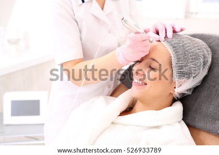 Beautician performs a needle mesotherapy treatment on a woman\'s face