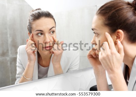 Reflection in the mirror.\
Woman looks in the mirror noticing the first wrinkles