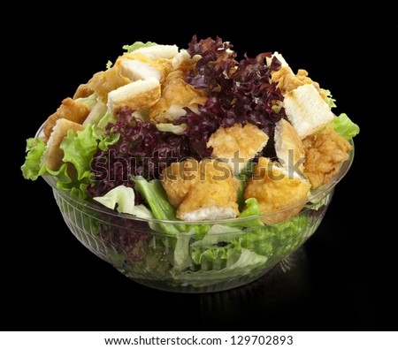Salad with chicken and fresh lettuce on black background in transparent bowl
