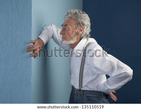 old man with a white shirt has placed his hand on blue wall