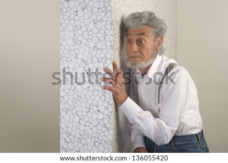 old man with a white shirt turn to a white wall and put his hand on the wall