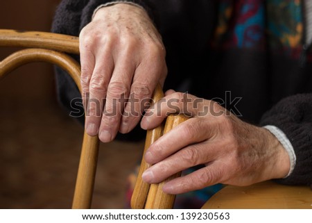 two hands of an elderly man lying on the back of a chair