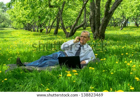 An elderly businessman is working the summer in the park using the Internet and telephone