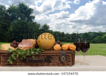 Fruit, wine, ham, cheese and basket in a forest