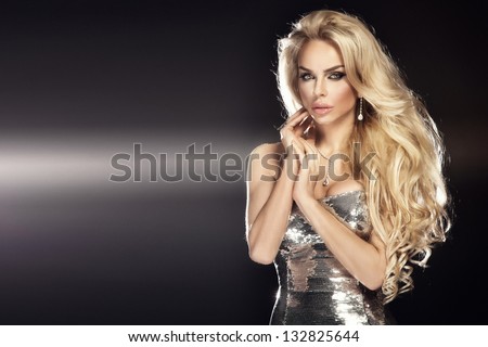 Fashion picture of beautiful young blonde woman wearing glitter silver dress. Long healthy curly hair.