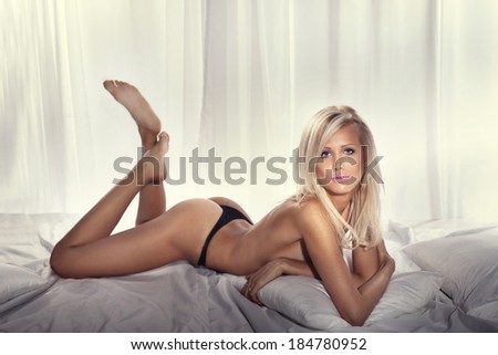 Sexy delicate blonde woman lying in big bed, relaxing, looking at camera. Lady with perfect body.