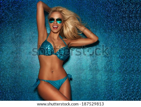 Sexy blonde woman posing in fashionable swimsuit posing on blue summer background