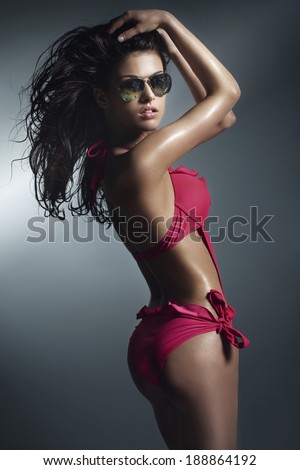 Sensual brunette woman posing in pink swimwear , wearing sunglasses. Studio shot