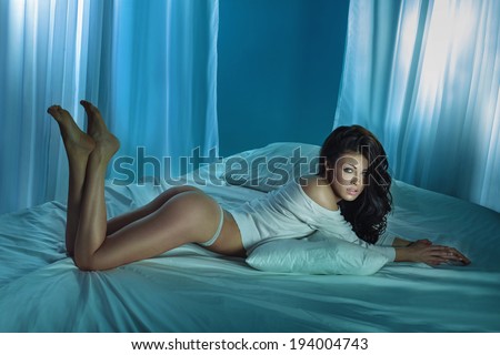 Sexy tanned brunette woman lying on big white bed, posing.