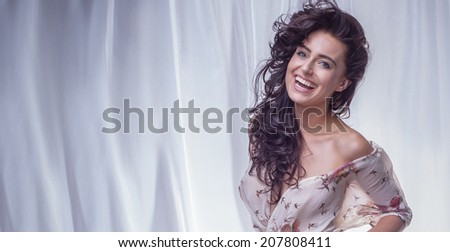 Happy beautiful brunette woman with long curly hair and amazing toothy smile posing, looking at camera.