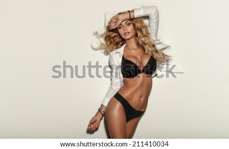 Sexy elegant blonde woman posing in lingerie in studio. Long curly hair. Sensual look. Fit body