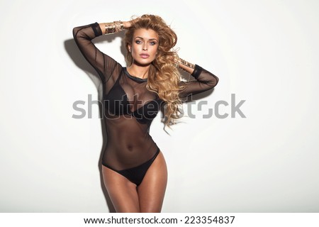 Sexy attractive blonde woman with perfect slim body posing in black lingerie, looking at camera. Girl with long curly hair.