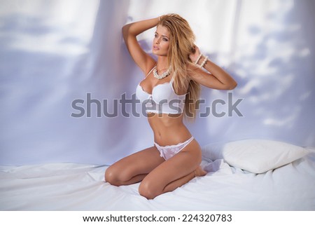 Sensual beautiful woman with perfect slim body posing in bedroom wearing white sexy lingerie.