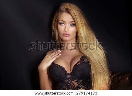 Sensual attractive blonde woman posing in bedroom, wearing black sexy lingerie. Girl looking at camera.