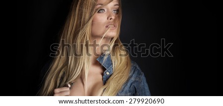 Portrait of sexy blonde woman in jeans shirt. Girl looking away. Black background.