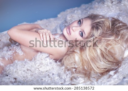 Delicate sensual naked woman lying in feathers. Blonde girl like an angel.