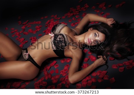 Sexy elegant brunette woman lying over red rose petals, wearing sensual lingerie.