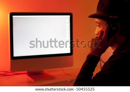 young man standing in front of a desktop computer holding cell phone