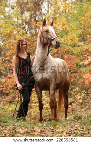 Nice girl with long hair standing next to amazing horse with halter in autumn