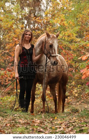 Nice girl with long hair standing next to amazing horse with halter in autumn