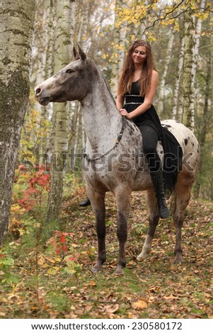 Young girl with appaloosa horse in autumn forest